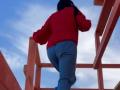 Nalini, con un maglione rosso e pantaloni blu, che sale delle scale di legno, vista posteriore, glutei leggermente sollevati, lunghi capelli neri, cielo blu sullo sfondo, ripresa da un'angolazione bassa..