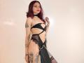 Amuneet with pink hair, tattoos, black strappy lingerie, chain, black bow, exposing tits and pussy, standing, looking at camera, white wall, sexy, confident, slim, pale skin.