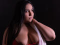 SalomettX with long black hair, brown eyes, and medium skin, wearing red lace and a white draped top, showing big boobs, hand on neck, dark background, soft smile.