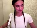DrusillaMaiava with braids, white t-shirt, and white shoulder bag, looking down with a small nose piercing and pink lipstick. She has a cute, sexy face.