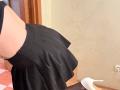 La gonna nera di EmmaNoa è sollevata, mostrando il suo sedere scoperto e il tacco alto bianco. Indossa calze nere che arrivano fino alla coscia, e il suo perizoma nero è visibile..