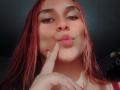 AntoniaBrunni with red hair, pouting lips, and index finger touching her lower lip. She has long eyelashes and a slightly tanned, smooth skin. Her pink pout is cute.