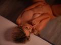 CandyCadbury, nue, allongée sur le dos avec ses cheveux blonds, de petites seins, et une bague à l'annulaire, touchant ses lèvres, dans un éclairage doux et chaleureux..