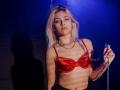 DataSley with platinum blonde hair, wearing a shiny red bra, holding a chain, shadow on dark wall, blue light, looking slightly to the side, sexy, slim, small tits.