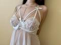Tisia's tits are in a sheer white lace babydoll with ribbon straps and tiny pearl details. Her arms are behind her back, wearing a delicate chain necklace.