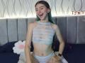 AbbyHillsI with blue-green hair, smiling, wearing a white lace cut-out bra and matching panties, showing a slim body and small tits, has a tattoo on her right shoulder.