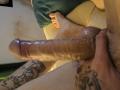XBobyNightX's erect, circumcised cock is in the foreground, showing a shiny, veined, flaccid-to-erect penis with a hand gripping the base. XBobyNightX's tattooed leg is in the background.