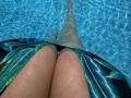 Barbarica's legs in a blue-green patterned swimsuit, water droplets on her skin, submerged in clear blue pool, legs stretched out, visible from a lower angle, thighs in focus.