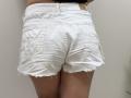 Tilliana's white, frayed, denim shorts with two pockets, slightly worn, showing her bare, tan-ass. She's standing with her back to the camera, in a minimal setting.