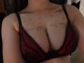 DarylSanks with large tits wearing a red and black lace bra, showing tattoos of stars and branches on her chest. Her skin is light, and her bra is slightly visible.
