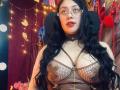 CristalZafiro with long black hair, glasses, and brown leather lingerie showing her big tits and cleavage. She's wearing a choker and has a surprised expression.