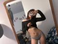 SpencerLe, vêtue d'un haut noir à une épaule, le soulève pour montrer ses abdominaux tonifiés, porte des sous-vêtements gris, prend un selfie devant un miroir avec son téléphone, révélant son corps mince et sexy..