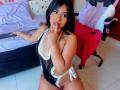 ZarayWhitMoreLove, with dark hair, wearing a black and white lace lingerie, finger to lips, sitting on floor, showing off her big tits and sexy ass. Bedroom setting.