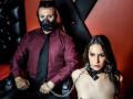 MasterNBun with a black mask and red shirt sits on a chair, chained, next to MasterNBun with brown hair, naked, wearing a black collar. Both look serious.