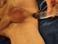 XBobyNightX's hairy scrotum and pinkish testicles are being gently inserted with a translucent dildo by their hand. Blue fabric is underneath XBobyNightX.