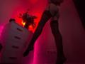 Silhouette of Tsukerberg with legs raised, wearing black thigh-high stockings and garter belt, against red and pink neon light. Fire-like glow behind white dresser, plant on top. Sexual tension.