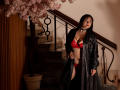 CamilaMoretti stands in red lace bra and panties, black leather coat, black choker, with black hair, looking at camera, near stairs, next to pink cherry blossom tree.