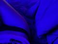 TenerliRize's butt in black underwear, illuminated by blue light, with a crumpled bedsheet to the right. Her skin is glowing under the light.