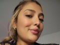 BiancaRey's face with light brown skin, blonde ponytail, thick eyebrows, glossy pink lips, small nose, wearing gold hoop earrings, smiling slightly, close-up shot, soft lighting.