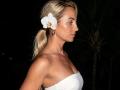 ViktoriiaLu has blonde hair in a ponytail, a white orchid in her hair, and wears a strapless white dress, showing her tits and bare shoulders at night.
