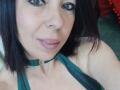 LauraSin with dark brown eyes, medium-length black hair, green choker, and green halter top, showing her boobs and pink lips in a selfie.