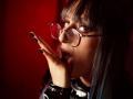 TatsumiLee with dark hair, bangs, and red glasses, tongue out, fingers with black nail polish, glossy black shirt, looking seductive, red background, intimate, sexy.