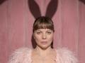 VeronikaGoldy has light brown hair in bangs, blue eyes, and wears a pink feathered top with a silver necklace, looking straight at the camera with a neutral expression.
