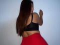 LinaFoxyHot with long brown hair, black sports bra showing her ass, and red skirt, looking over her shoulder with a slight smile.