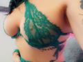 FrenchShanna's tits in a green lace bralette, showing a tattoo on her side, black hair, green wristband, and a partial view of her pink panties.
