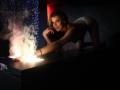 EvieBliss, on all fours, with white panties, leans over a table with a flame, her ass raised, blonde hair, seductive expression, dark room, Brazzers watermark.