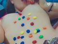 Les seins nus d'IvannaSinn sont couverts de morceaux de bonbons colorés, et ses ongles peints en rouge sont près de sa bouche. Icône de cœur et points de suspension en haut à droite..