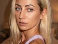 ViktoriiaLu has blonde hair, blue eyes, and a serious expression. She's wearing a light purple tank top, showing her bare shoulders and subtle makeup. Her ass is not visible.