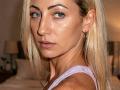 ViktoriiaLu has blue eyes, blonde hair, and a serious expression. She's wearing a pink tank top, and her shiny, freckled face is turned slightly to the camera.
