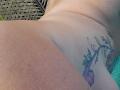 FrenchieLilieFleur's wet ass with a colorful flower tattoo on the right buttcheek, water droplets visible, lying on a green surface.