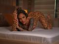 ExoticTala liegt auf einem Bett, trägt einen Body mit Leopardenmuster, hat das Gesäß angehoben und Tattoos am Arm. Sie schaut in die Kamera, ihre Nägel sind rot lackiert..