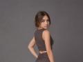 BessBetak has small tits, a slim ass, and brown eyes. She's wearing a sleeveless, brown, midriff-baring top with matching bottom, standing with a hand on her hip.