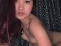 Nude DomoniqueBielefield with medium tits, light brown skin, and long purple hair, wearing a heart necklace, looking at the camera with slightly pouty lips.
