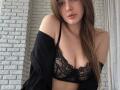 Lelliana with long brown hair, looking at the camera, wearing a black lace bra that shows her tits, and a black off-shoulder shirt. She has a cute face.