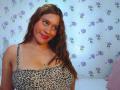 BelletinaXx with wet brown hair, wearing a leopard-print top, showing her big tits, smiling with pink lipstick, against a floral wallpaper.