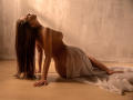 KarlaSoto, topless, with long brown hair, leans back, arms on floor, white cloth covering her ass, wooden floor, soft lighting, sensual pose.
