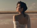 OliviaCluff with short dark hair, wearing a white off-shoulder top, black halter, and showing her bare back, looking to the side with a calm expression.