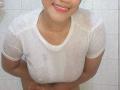 IvannaDuran with wet white shirt, visible nipples, small breasts, smiling, hands on lower belly, pink lipstick, short hair, tiled wall background.