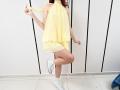 JuliannaMoor with pale skin, red hair, yellow halter dress, white sneakers, and one leg crossed, holding dress strap, standing on white tiled floor.