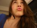 PeacHub69's pouty pink lips are puckered up, looking up with blue eyes, brown wavy hair, and a blue shirt, showing off her soft, fair-skinned face.