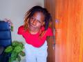 KharlaQueen with dark skin, dreadlocks, red top, and white pants, leaning against a wooden door, smiling slightly, looking up. Her tits are small, and she's cute.