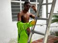 Shirtless DrakeWit with dark skin, wearing black sunglasses, bright green jacket, and yellow gloves, standing by a metal ladder, exposing a flaccid, uncircumcised penis.