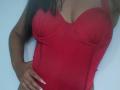 SheilaBrunette wearing a red, underwire, bust-enhancing, tight-fitting top, showing her tits, with long dark hair, hand on her hip, and light skin.