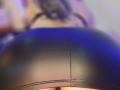 Kkole's shiny black ass in tight leather shorts, highlighted by a blue light, with a subtle view of her lower back and a hint of her upper body.