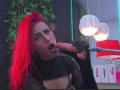 AlissaBrown with bright red hair, black sheer top, and open mouth, sucking a large, uncircumcised, erect penis, holding it with a black cloth.