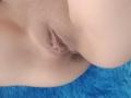 A vulva de SharonKm está no centro da imagem, com suas nádegas à direita e uma superfície azul e felpuda abaixo. O foco está em sua vulva..